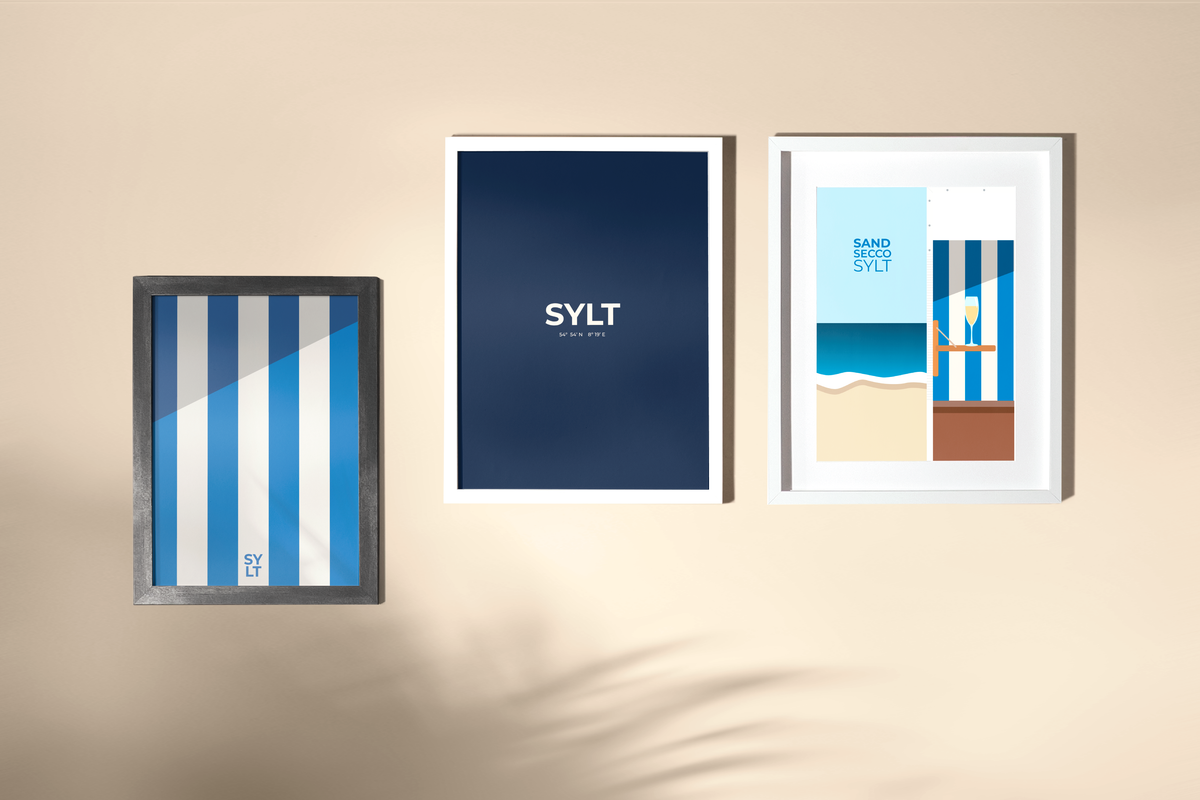 Das Sylt Typografie-Poster in der Mitte einer gerahmten Dreierhängung mit den Sylt Postern Strandkorbstreifen und Sand Secco Sylt aus der Launch Kollektion. 