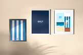 Das Sylt Typografie-Poster in der Mitte einer gerahmten Dreierhängung mit den Sylt Postern Strandkorbstreifen und Sand Secco Sylt aus der Launch Kollektion. 